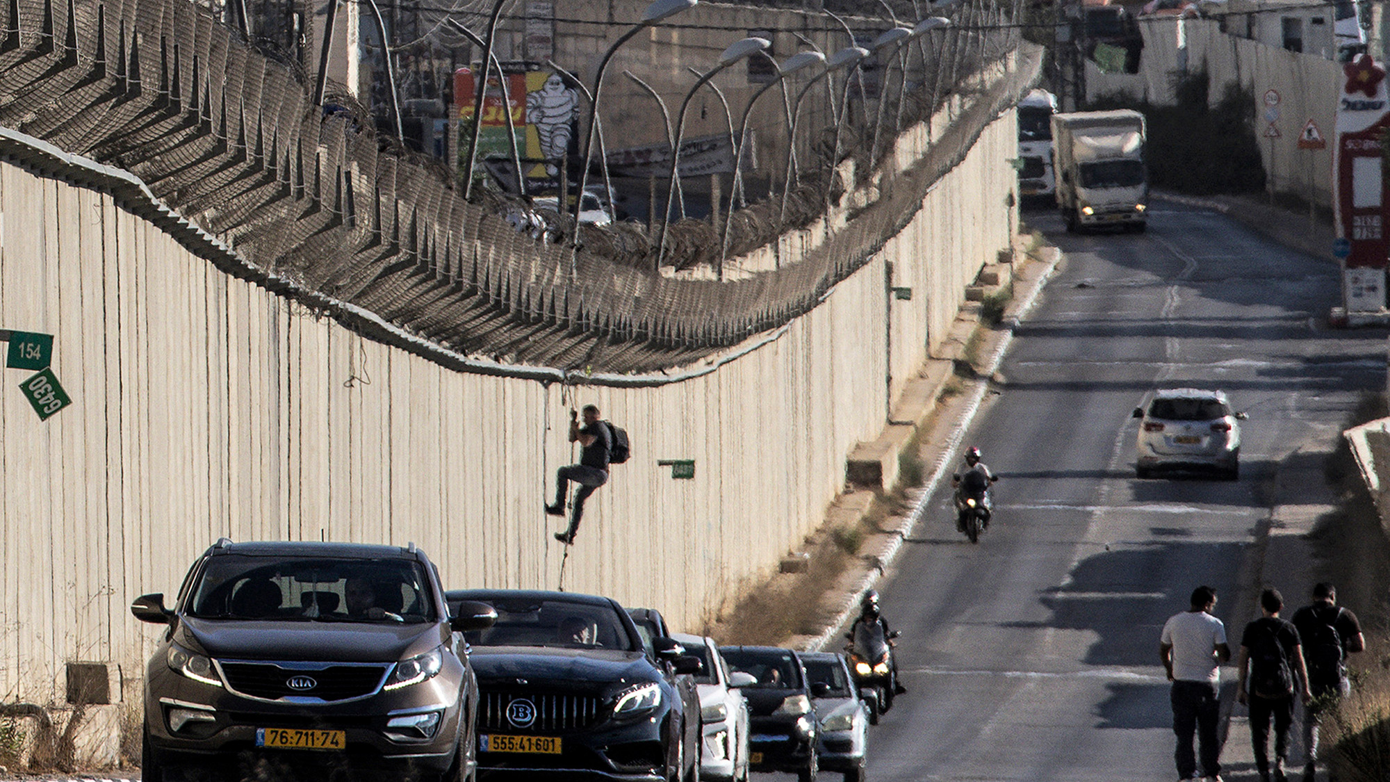 A man lowers himself while climbing down the Israeli side of the separation barrier with the West Bank near the Qalandiya checkpoint on 30 September 2024 (AFP/John Wessels)